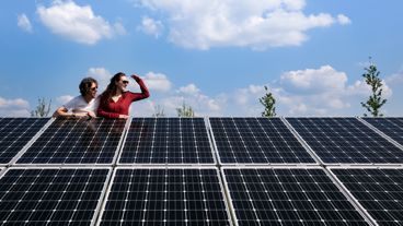 Twee mensen leunen over een rij zonnepanelen en kijken samen naar rechts. Met zonnepanelen maak je een stap naar de toekomst.